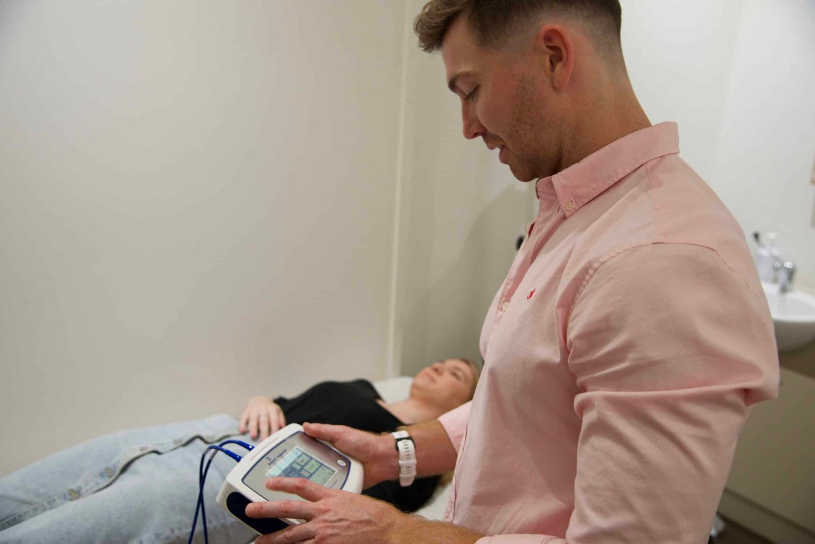 Naturopath standing next to female patient that's lying down while he checks her vitals at NXTLVL Health